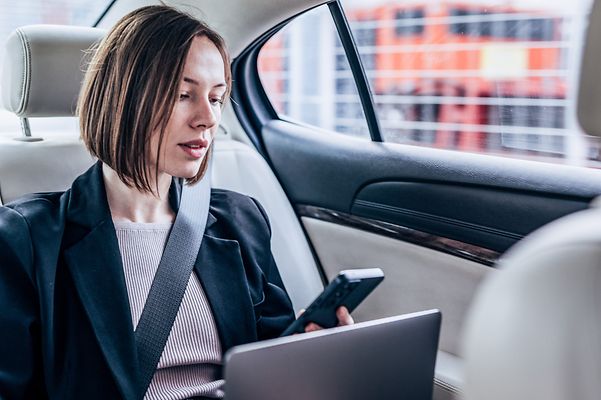Eine Frau sitzt im Auto und schaut auf ihr Smartphone.