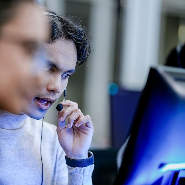 Person mit Headset arbeitet konzentriert an einem Desktop-Monitor in einer Büroumgebung.