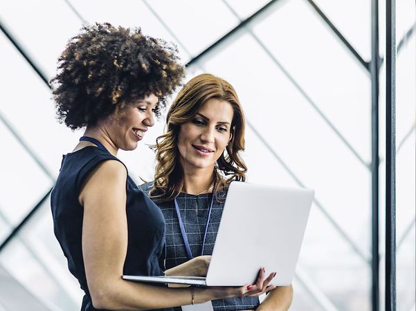 Zwei Business-Frauen blicken gemeinsam auf einen geöffneten Laptop, daneben ein Icon mit der Aufschrift „Modern Work“.