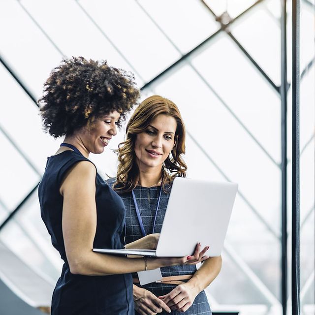 Zwei Business-Frauen blicken gemeinsam auf einen geöffneten Laptop, daneben ein Icon mit der Aufschrift „Modern Work“.
