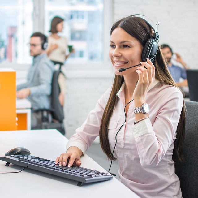 Frau mit dunklen Haaren und Headset beim telelefonieren am Schreibtisch per virtueller Telefonie dank SIP Trunk Company Flex