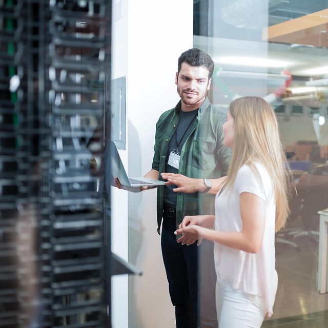 Eine Frau und ein Servicetechniker stehen vor einem Serverschrank und sprechen über Business LAN – Cisco