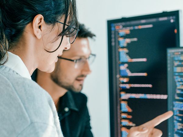 Ein Softwareentwicklungsteam vor zwei Bildschirmen ist mit der Problemlösung und Codeanalyse beschäftigt.