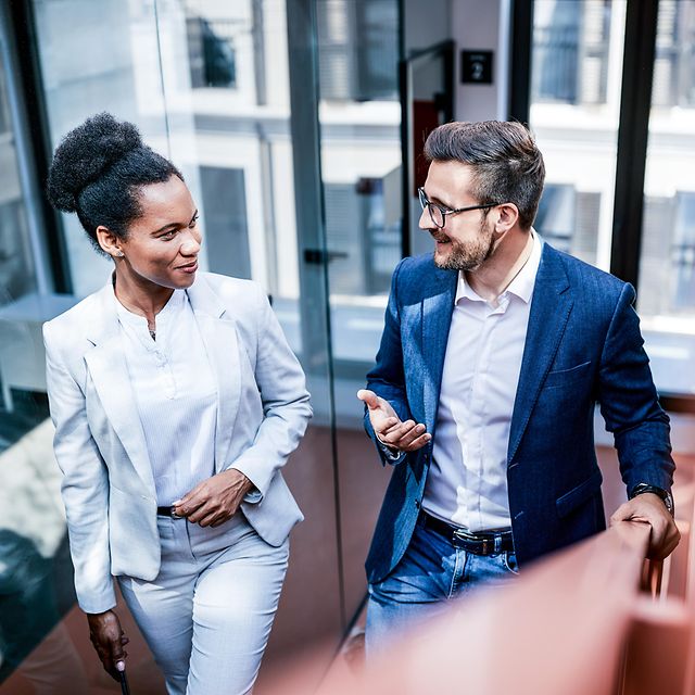Eine Frau und ein Mann in Businesskleidung unterhalten sich locker während sie eine Treppe hinaufsteigen