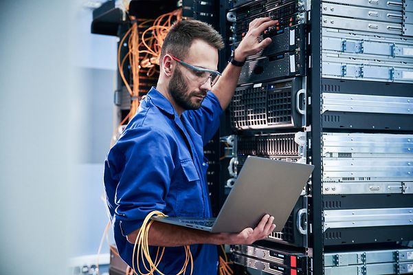 Servicetechniker mit Laptop in der Hand steht am Schaltkasten um Yealink W90 zu integrieren.