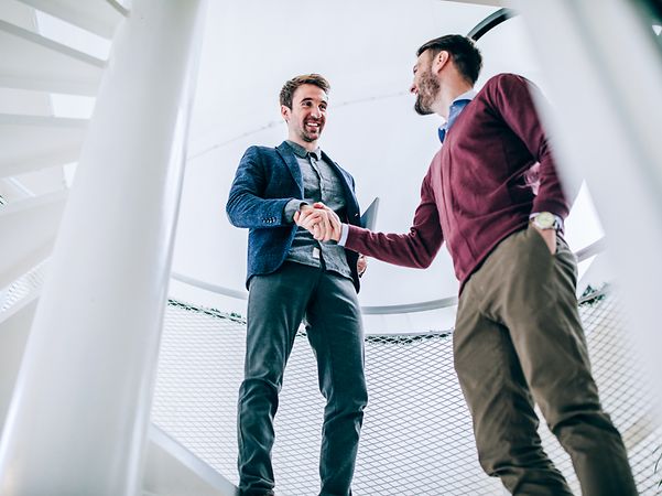 Zwei Männer in legerer Businesskleidung schütteln sich die Hand.