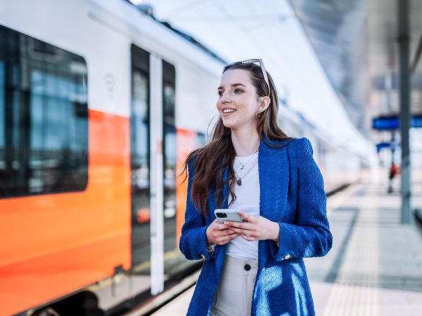 Eine Frau steht am Bahngleis und liest eine Nachricht, die über SMS Massenversand gesendet wurde