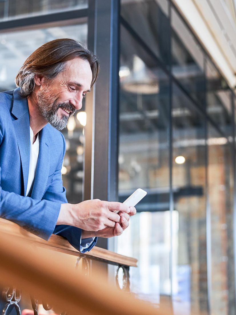 Mann im Businesslook schaut auf sein Smartphone und informiert sich über T Business.