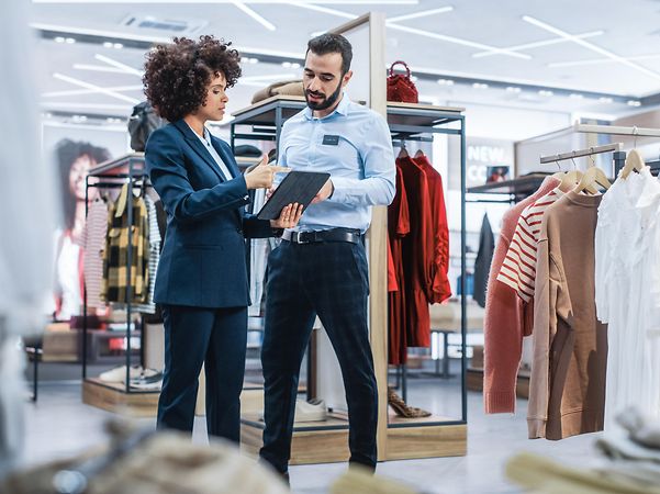 Führungskraft im Einzelhandel bespricht Strategien mit Mitarbeitendem – im Zeichen der T Business Mission